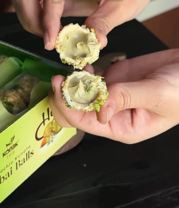 Person holding a split shell with dubai chocolate ball filled with pistachio and kunefe, with a blurred background