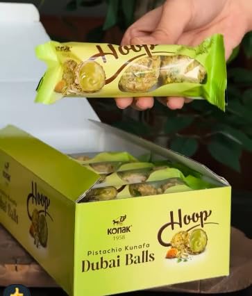 Hand holding a green package of Dubai Balls with a box of the product in the foreground.