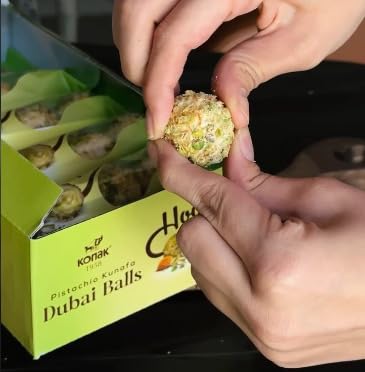 Person holding a Dubai chocolate Ball with a box of Dubai Balls in the background